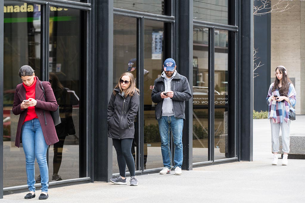 Customers practice social distancing as they wait outside a bank branch in Toronto in March 2020.