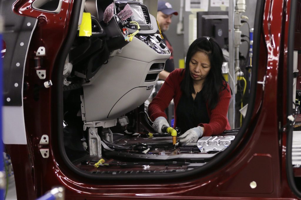 A factory employee works in the front-seat area of a Chrysler vehicle. The photo is taken through the vehicle's driver's side, which does not yet have a door attached.
