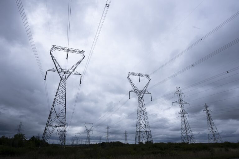 Four rows of towering pylons strung with high lines are silhouetted against dark, roiling clouds.