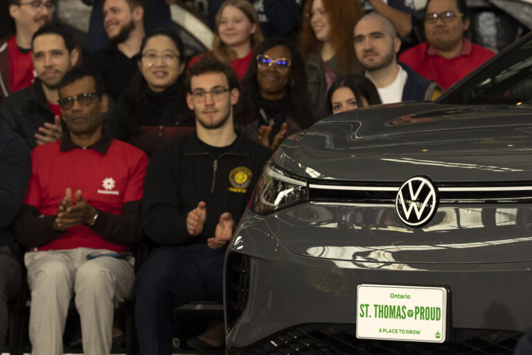 A volkswagen car with a number plate that reads, ‘St. Thomas Proud’ in green. A bunch of people are applauding in the background.