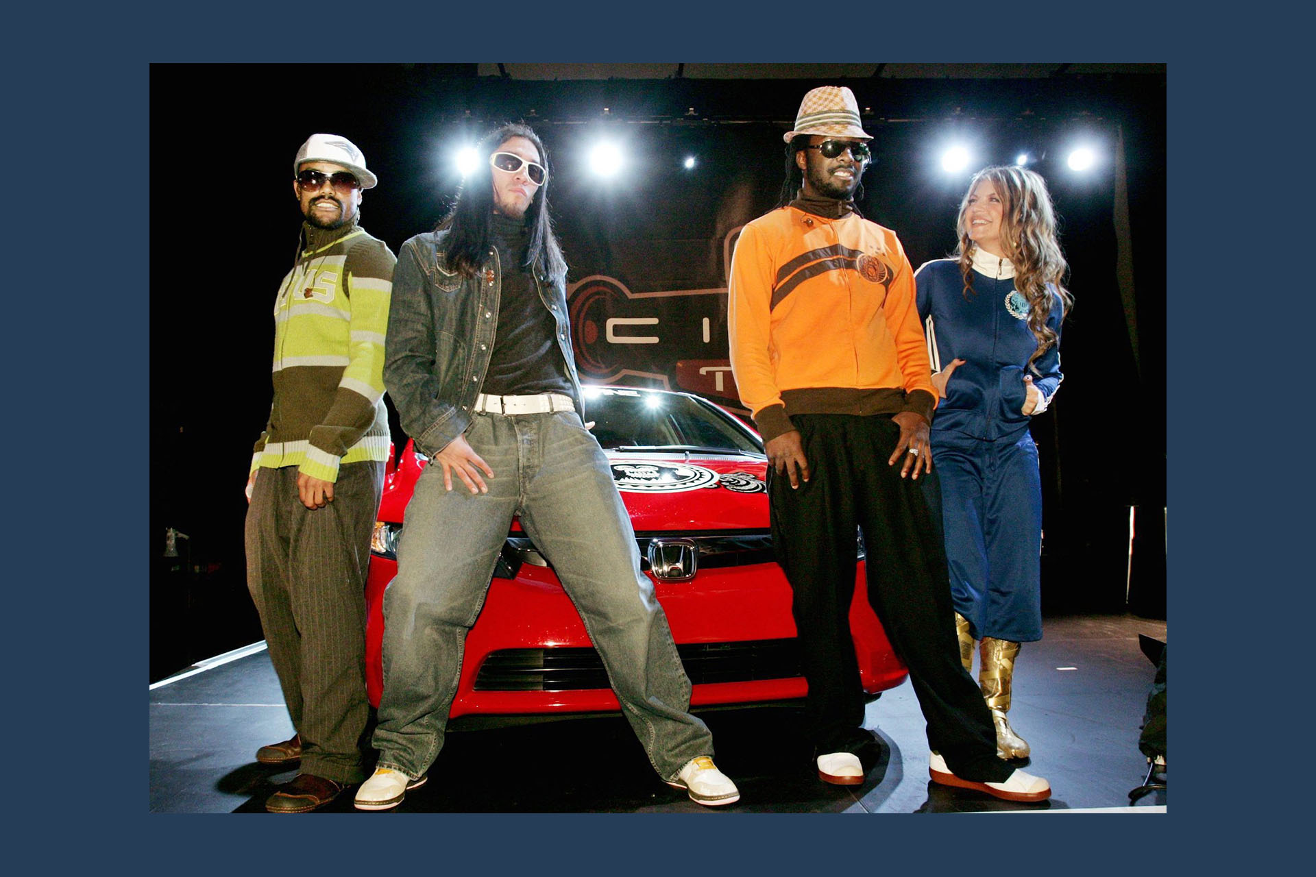 The four members of the musical group the Black Eyed Peas pose onstage with a red Honda Civic Hybrid car.
