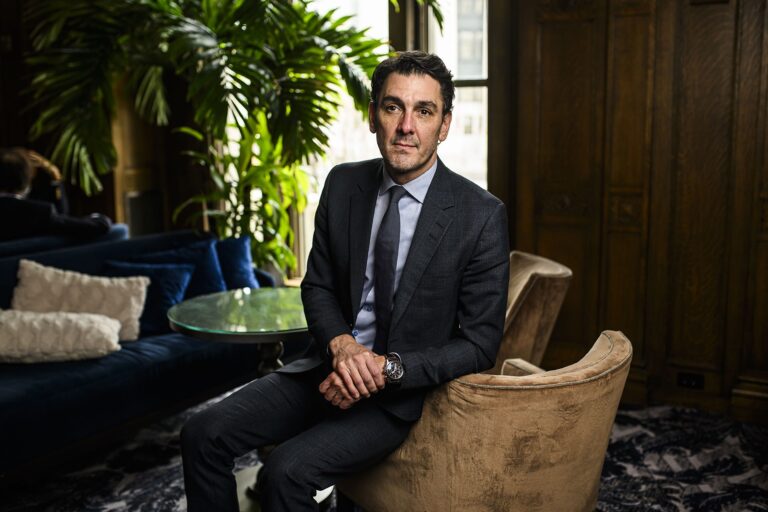 A photo of Martin Imbleau, head of Via Rail’s high-frequency rail project, wearing a grey suit, seated on the arm of a chair.