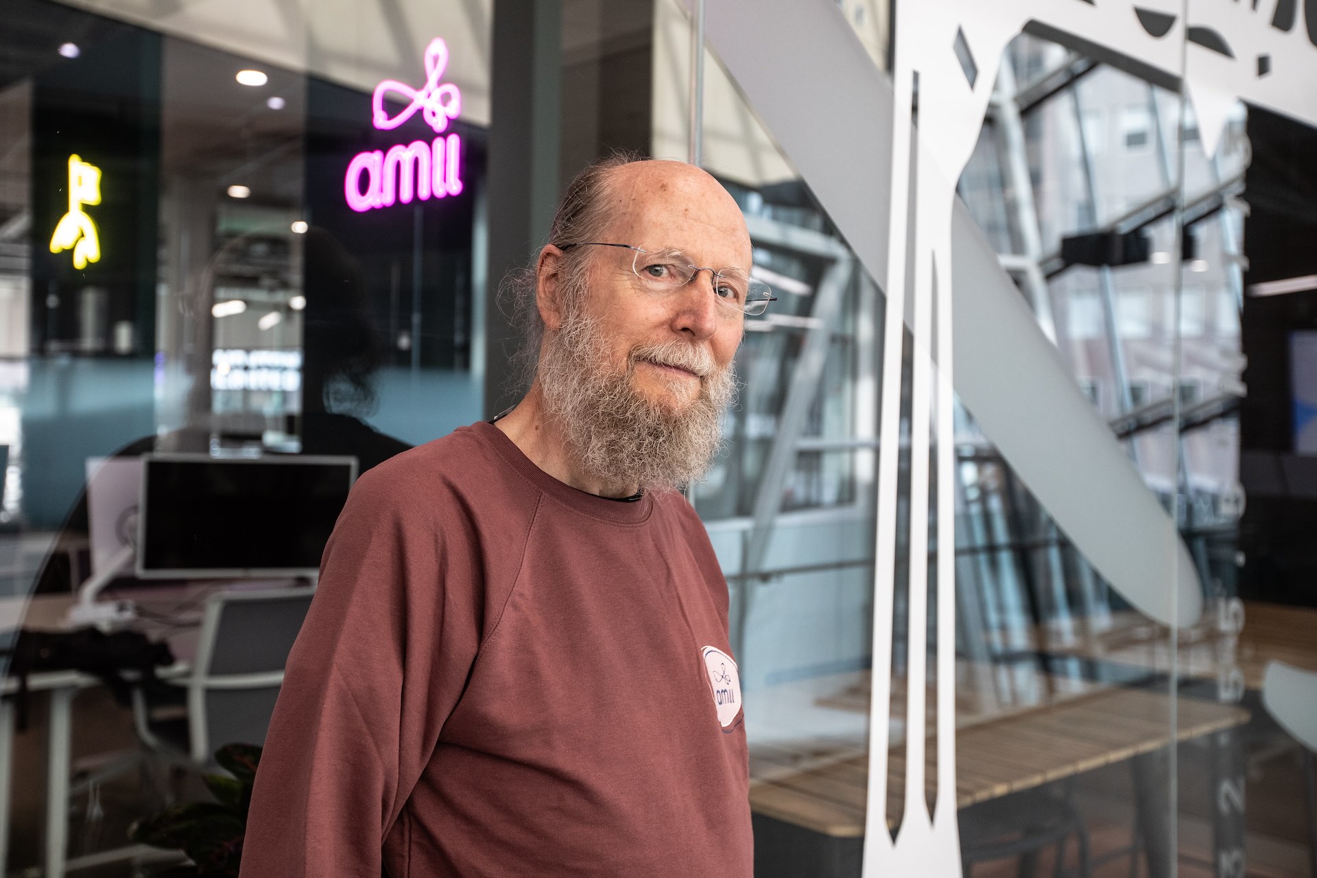A photo of research pioneer Richard Sutton with an “AMII” sign on a glass window in the background.