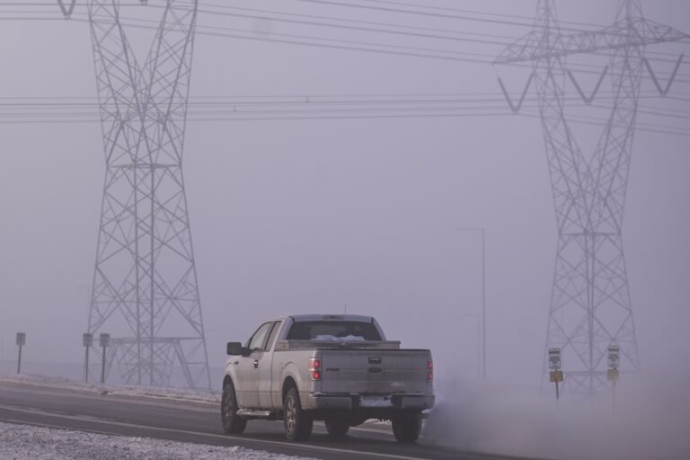 A network of electric poles with wires is seen at daytime with frost and ice fog around it.