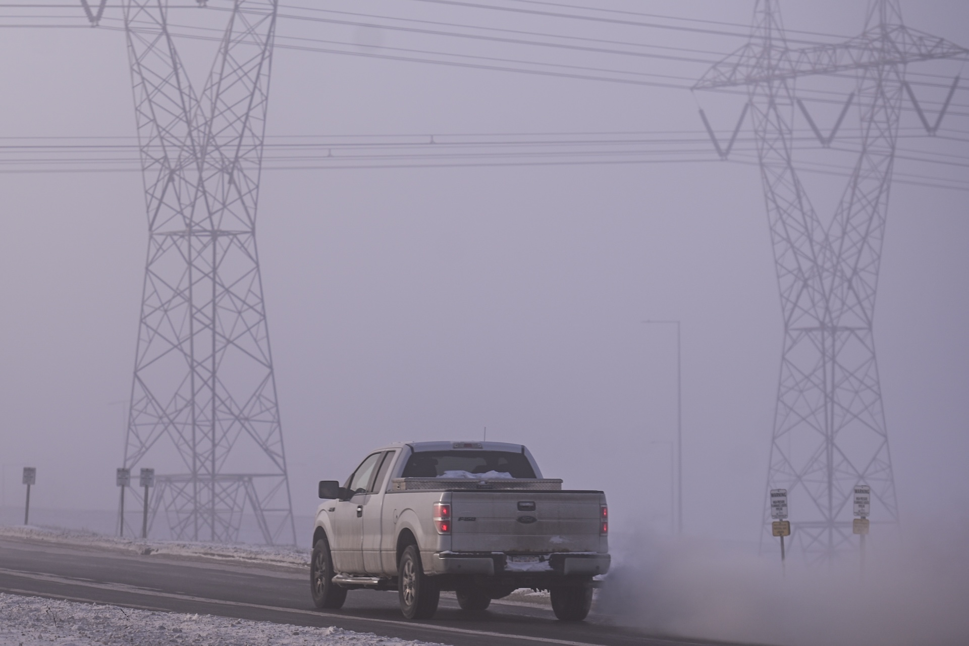 A network of electric poles with wires is seen at daytime with frost and ice fog around it.