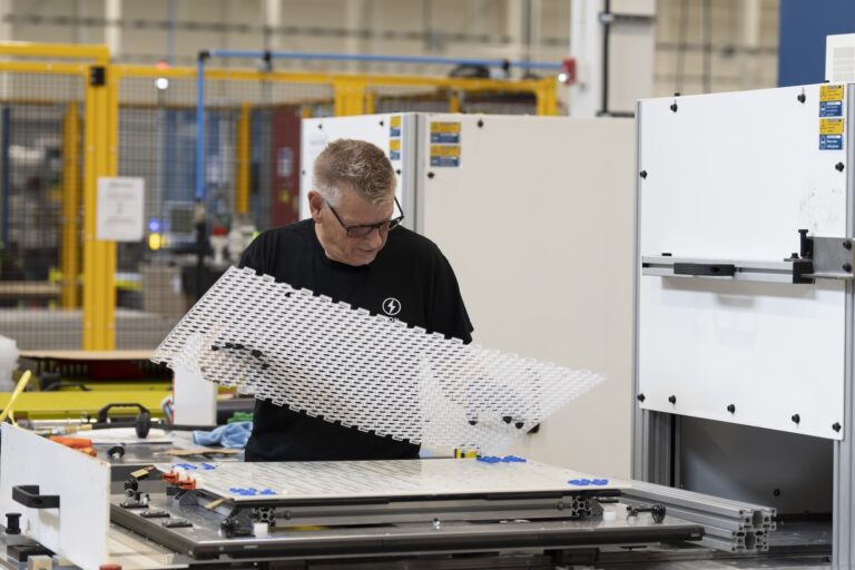 A factory worker holds a clear sheet with holes in it.