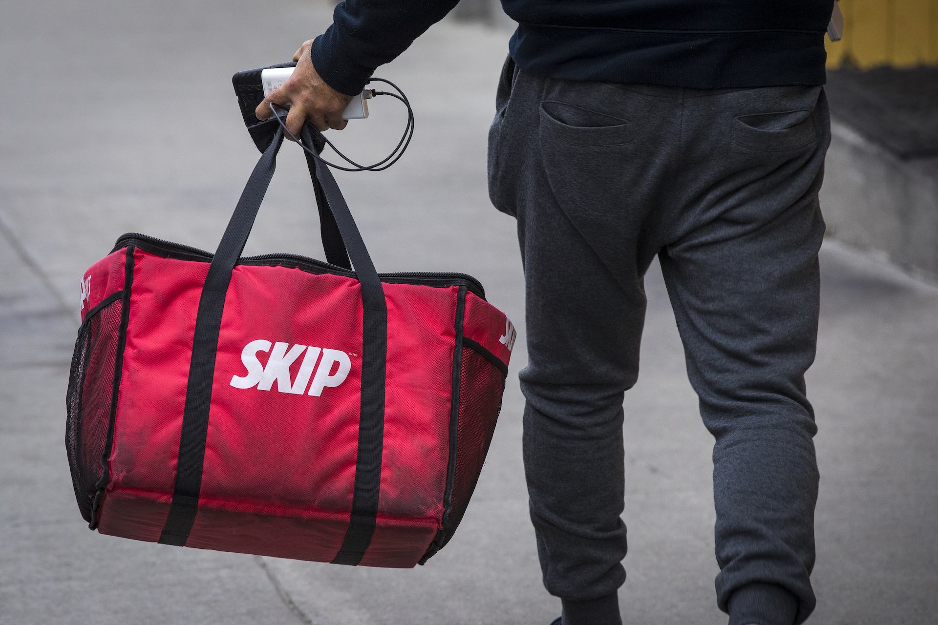 A person wearing grey pants carries an insulted red takeout food bag in their left hand.