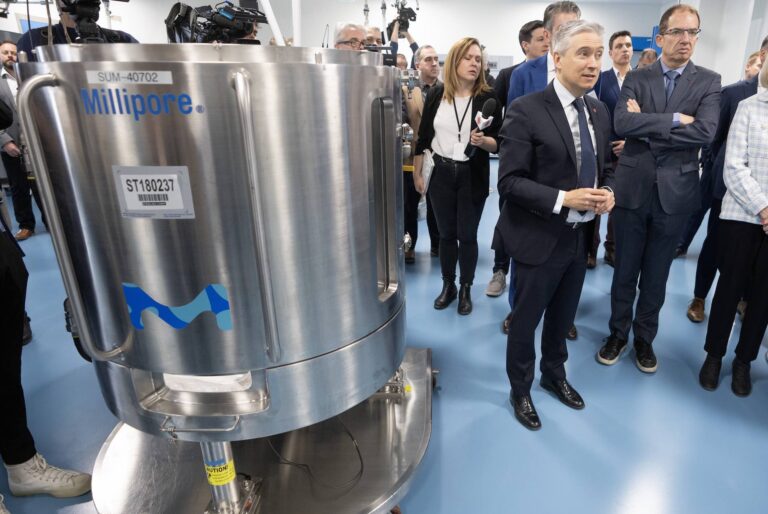 Moderna chief executive Stephane Bancel and Federal Innovation Minister François-Philippe Champagne stand to the right of a large silver vat during a Moderna facility tour.