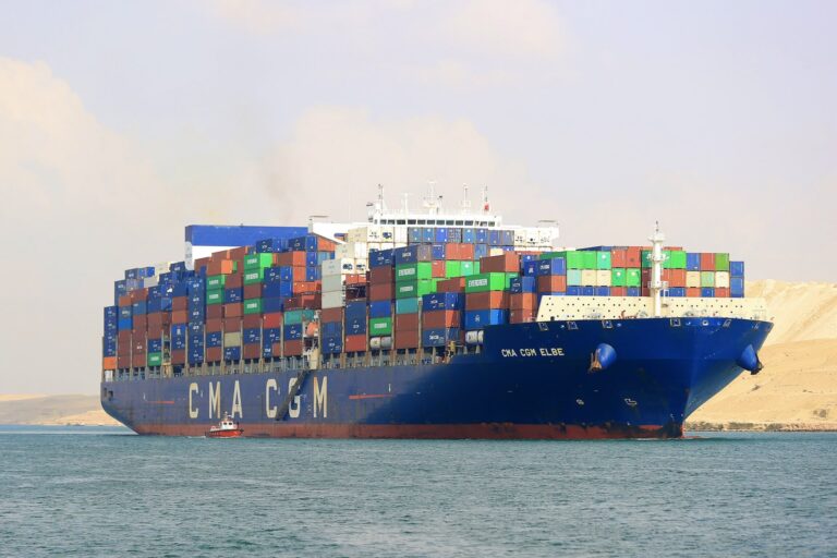 A blue-coloured cargo ship with orange, red, blue, green and white containers on sea. It has “C.M.A. C.G.M.” written over it.