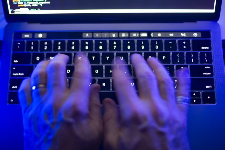A pair of hands type on a keyboard in a room with blue light.