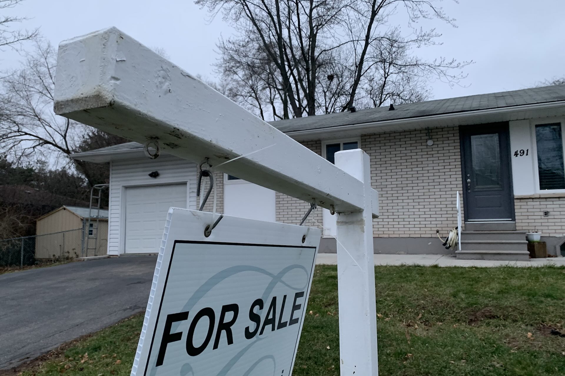 A white sign reading “FOR SALE” in front of a white-brick bungalow house in Toronto.