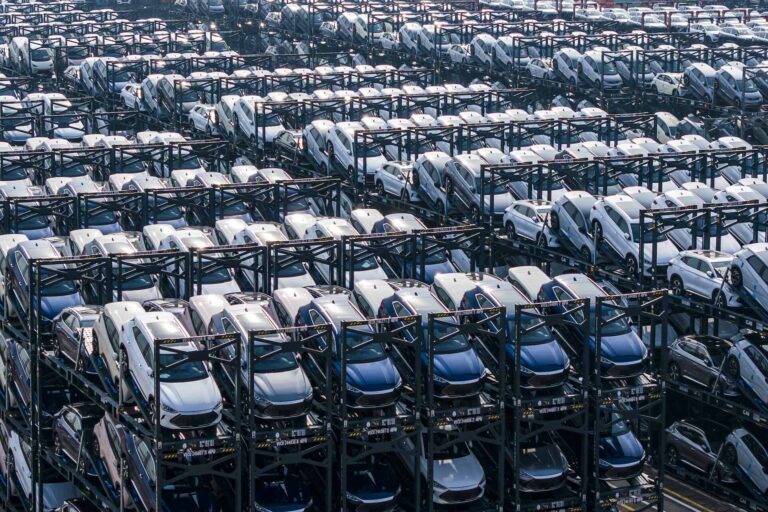 A high-angle shot of a sea of BYD cars awaiting shipment. The vehicles are on rack-like structures, each of which has three tiers holding cars.