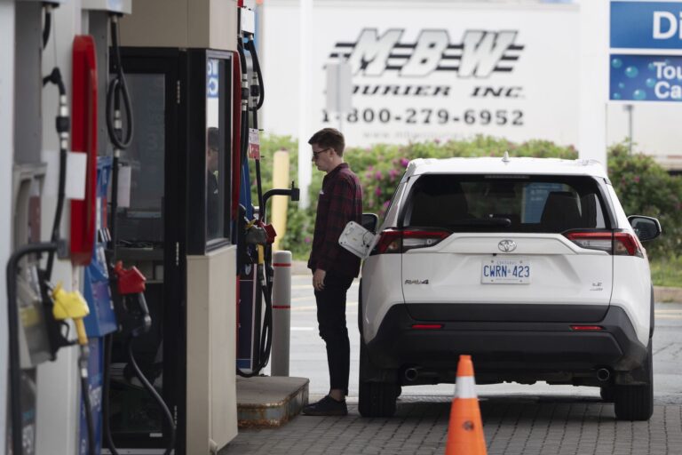 A person at a fuel pump stands to the left of a white Toyota SUV.