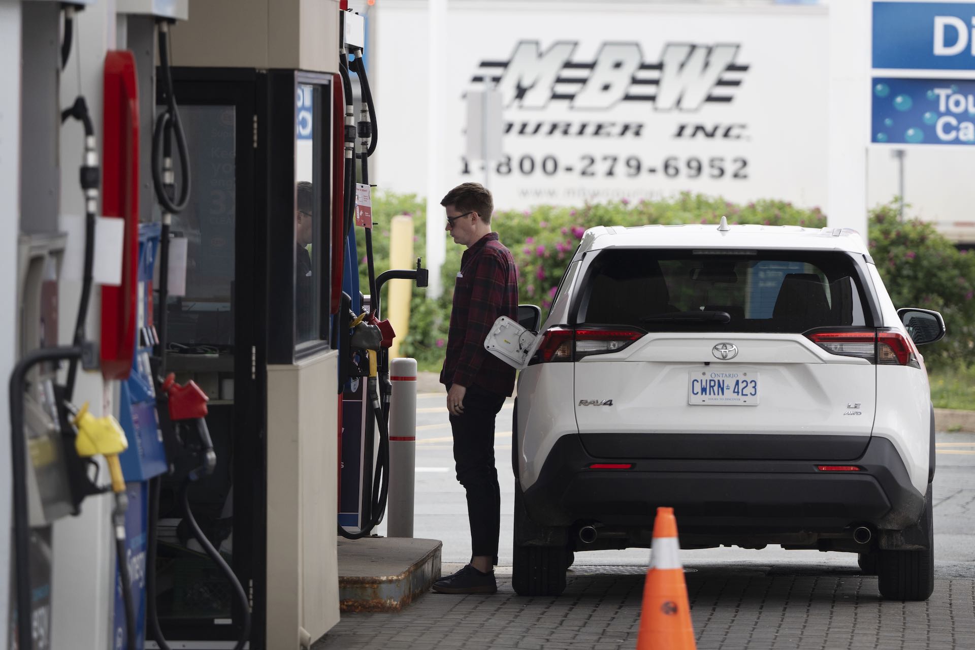A person at a fuel pump stands to the left of a white Toyota SUV.