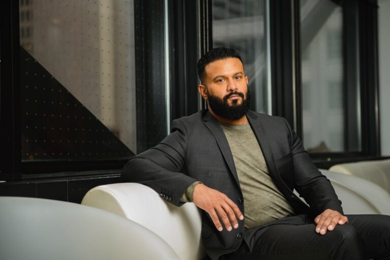 Lightspeed interim CEO Dax Dasilva sitting on a couch. He has a beard and is wearing a black suit with a green T-shirt.