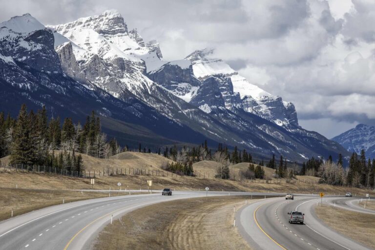 Three cars travel along the Trans Canada Highway, with Mount Rundle in the background.