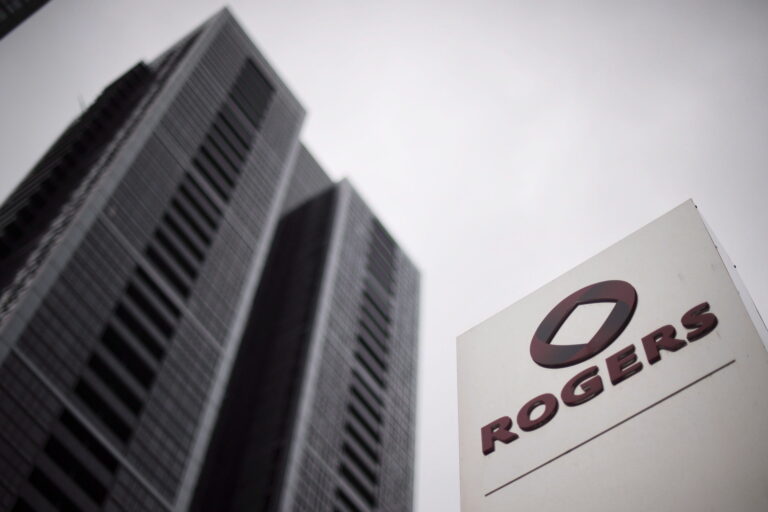 A photo of the Rogers logo on a sign in Toronto, with a soaring office tower in the background.