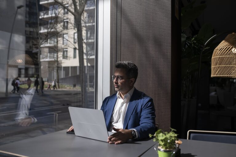 Symend CEO Hanif Joshaghani is sitting with a laptop in front of him, looking sideways into a window with a street view.