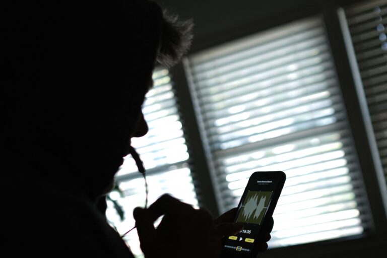 A silhouetted person uses a smartphone to record a voice message.