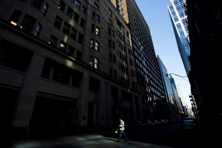 A shaft of light illuminates a man crossing a street within a canyon of dark office towers in downtown Toronto.