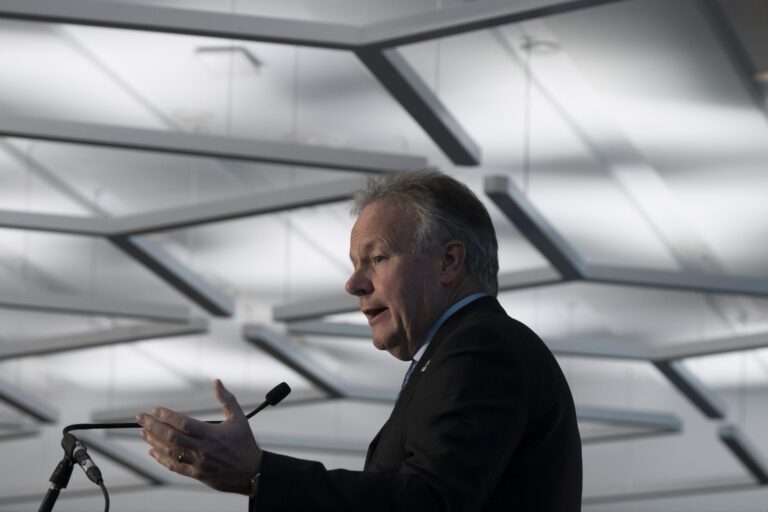 Former Bank of Canada governor Stephen Poloz speaking into a microphone, raising his left hand.