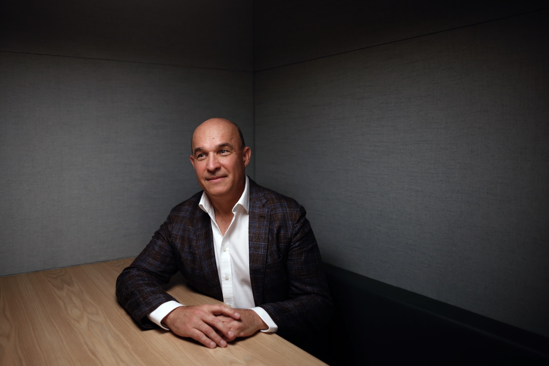 Former Research In Motion co-CEO and chair Jim Balsillie in a plaid suit jacket sitting at a wooden table in a dimly lit room, looking to the side.