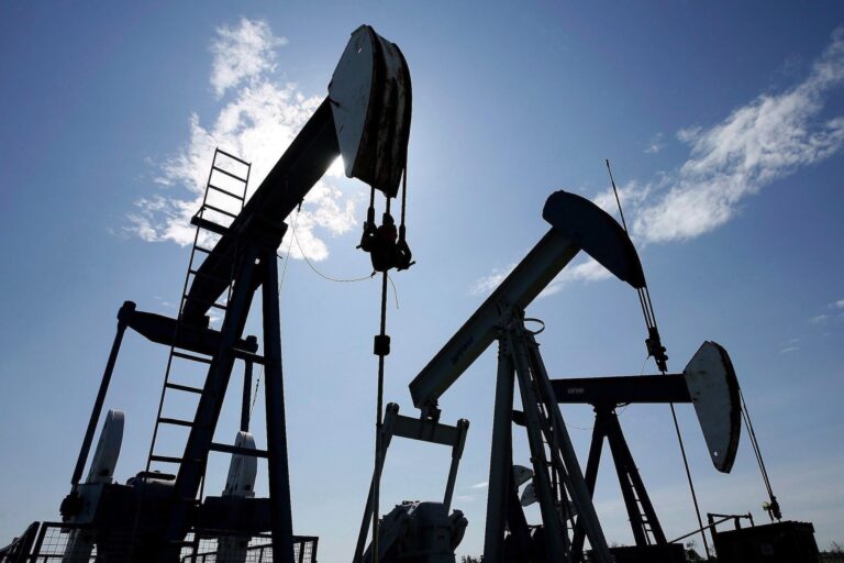 Three pumpjacks pumping crude oil on a field on a cloudy day.
