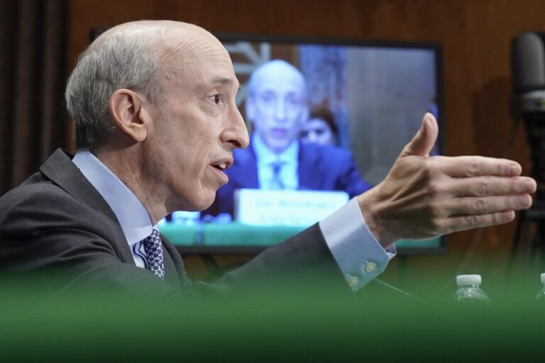 Securities and Exchange Commission Chair Gary Gensler sitting in front of a tv screen with live streaming giving a speech. 
