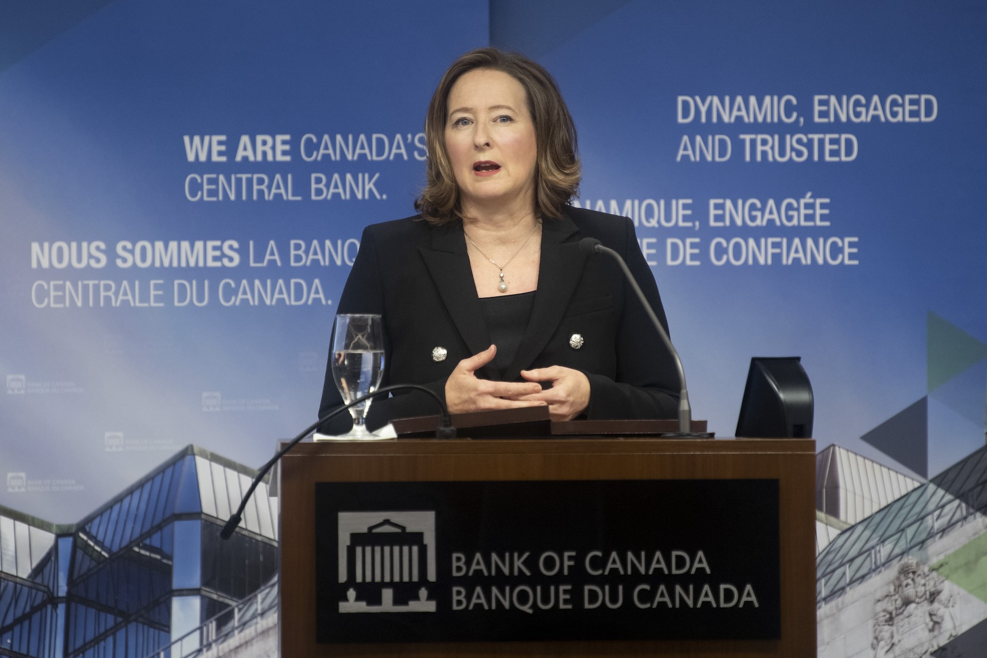 Senior deputy governor Carolyn Wilkins at a Bank of Canada podium in a black suit speaking into a microphone.