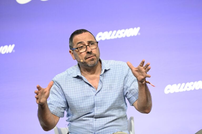 Cerebras CEO Andrew Feldman wearing glasses and a checkered shirt speaks into a microphone while gesturing with his hands against a purple background with "COLLISION" written on it.