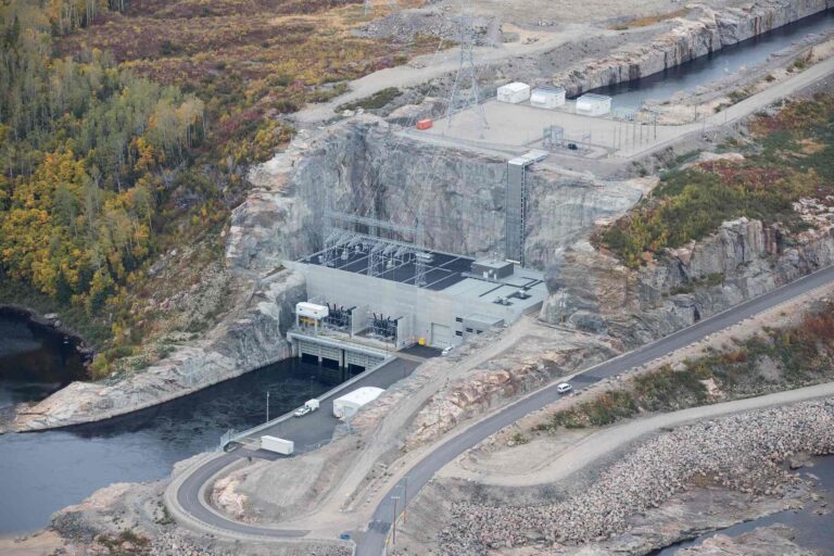 An aerial photo of a hydro-electric generating station in the grey, rocky terrain of eastern Quebec. The station sits at the end of a water-filled channel hewn into the rock.