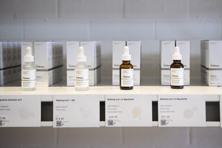 Rows of eyedropper bottles with plain, pharmaceutical-style labeling sit evenly spaced on shelves, before a white-painted brick wall.