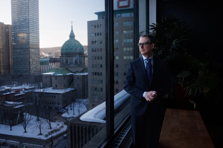 Tiff Macklem, governor of the Bank of Canada, looking out of a giant window with a view of city streets in Montreal.