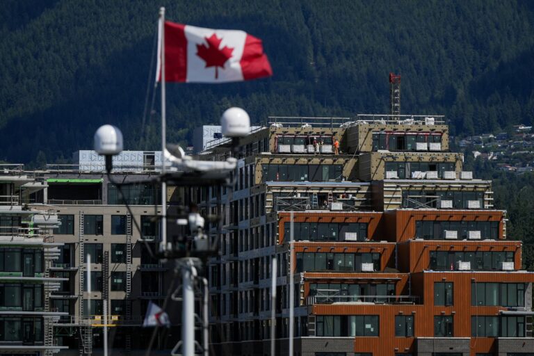 Construction workers are seen outside a condo development under construction as a Canadian flag flies from a mast on a boat.