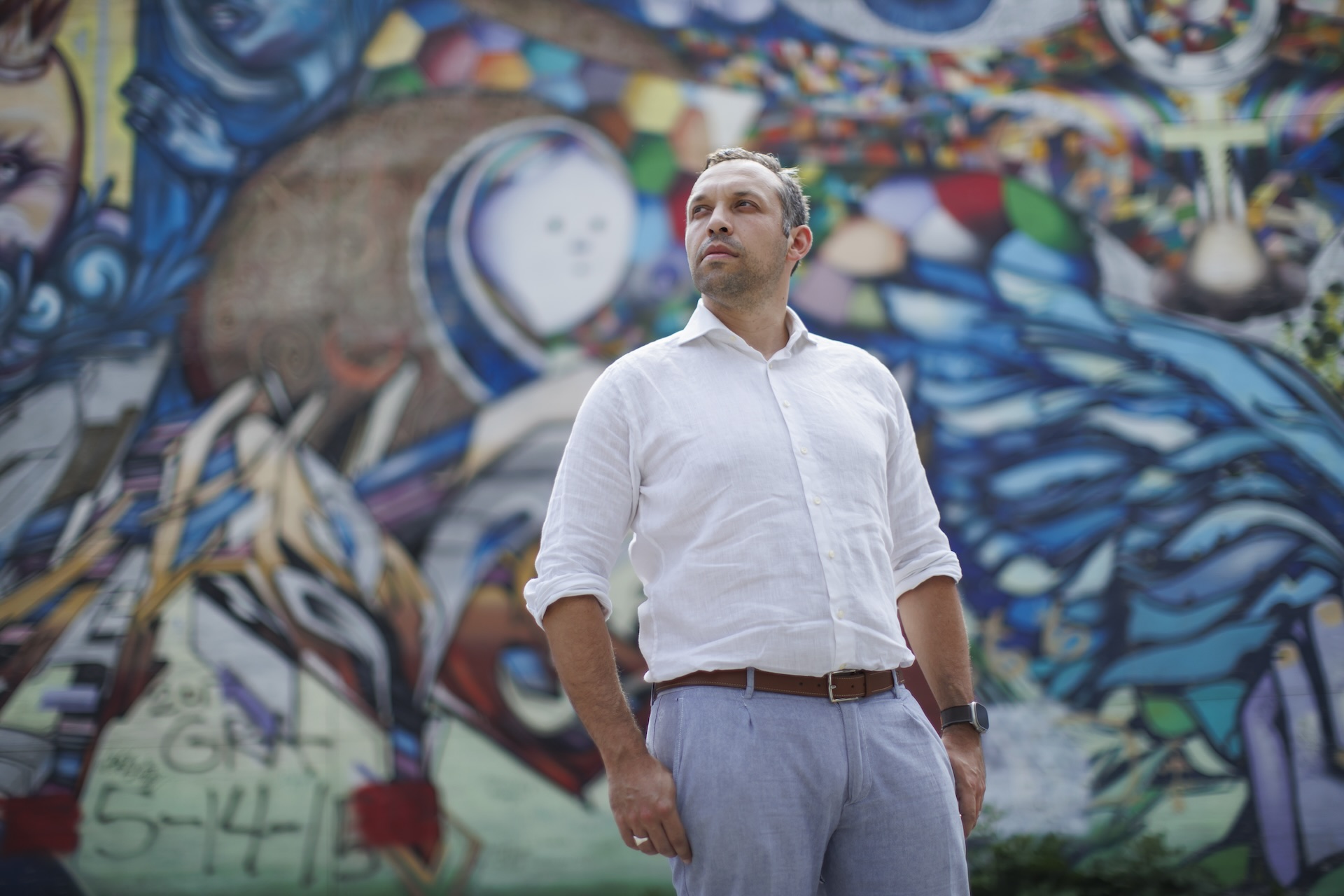 PharmAla CEO Nick Kadysh in a white shirt and pastel blue pants standing in front of a colourful graffitied wall.