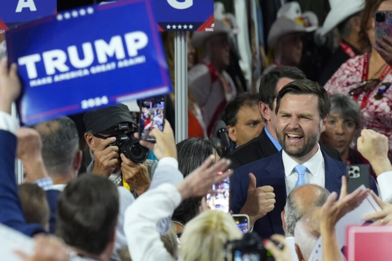 Republican vice presidential candidate J.D. Vance giving a thumbs-up to people surrounding him. There are blurred-out signs in their hands that read ‘Trump 2024.’