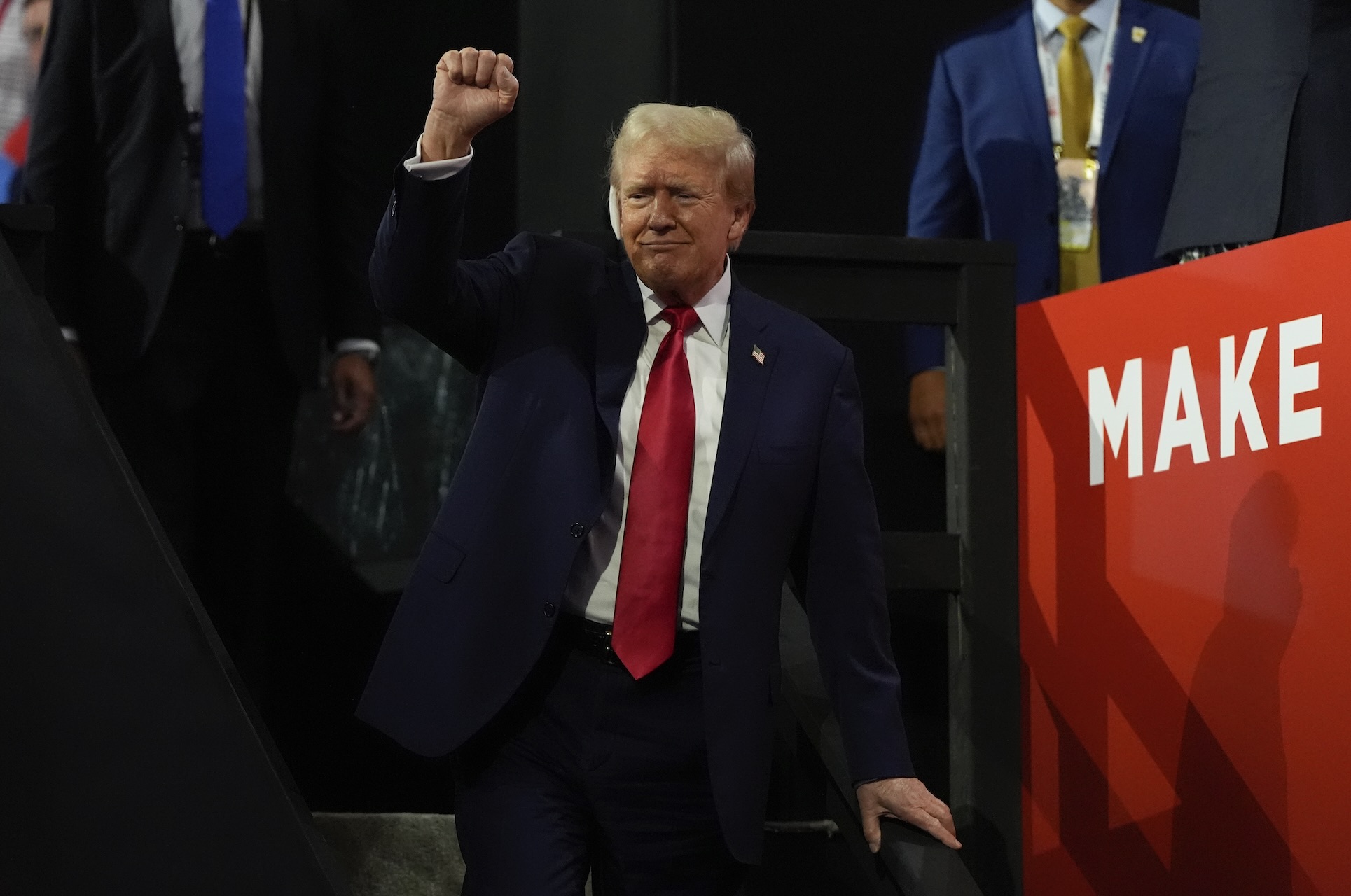 Republican presidential candidate former President Donald Trump in a black suit and red tie, raising up his right hand made into a fist.