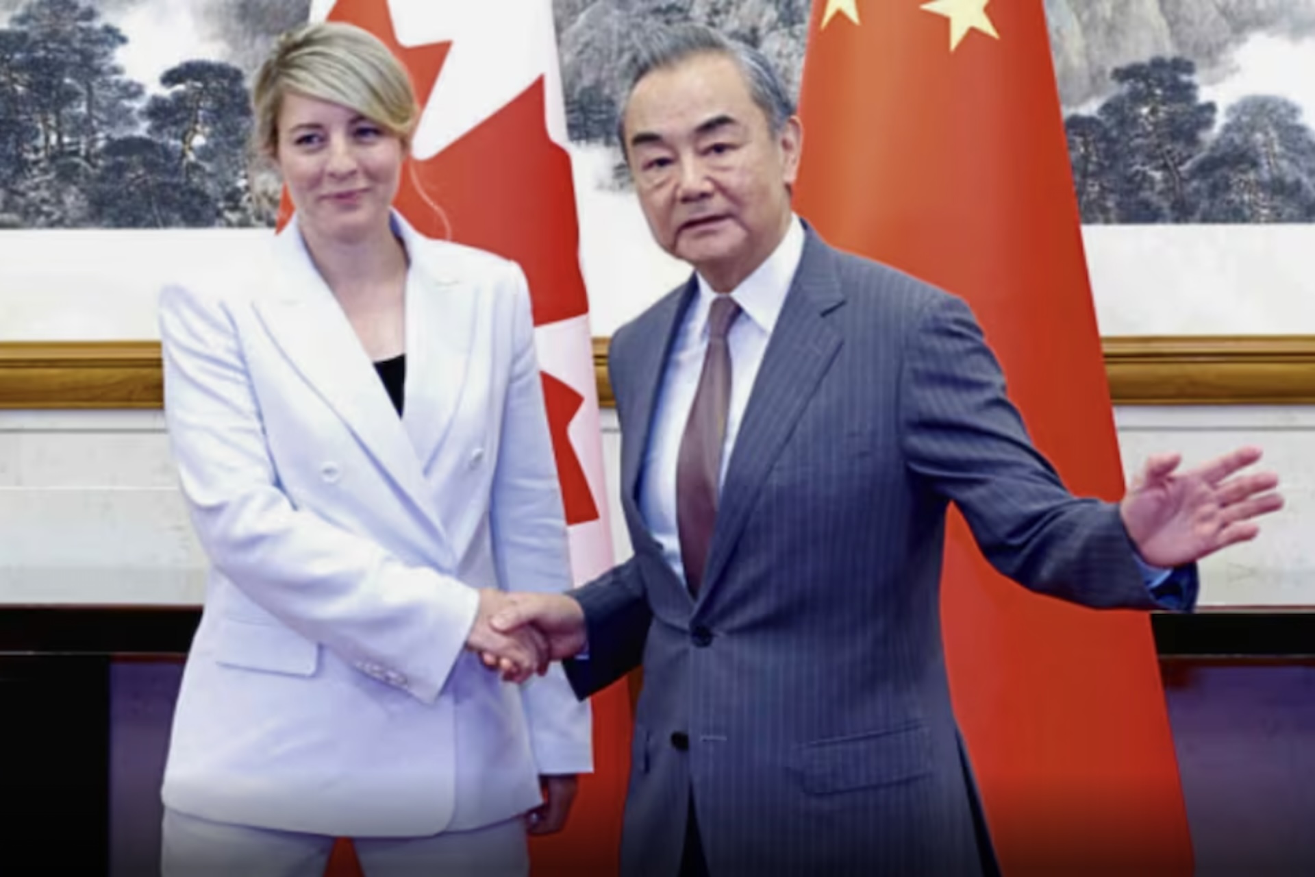 Foreign Affairs Minister Mélanie Joly in a white suit shaking the hand of China’s Foreign Minister Wang Li. Two Canadian and Chinese flags can be seen behind them.