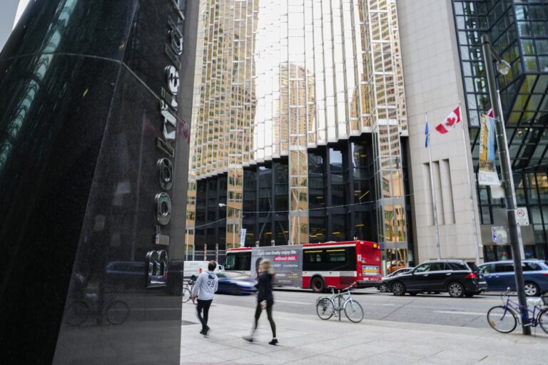 People walking past the building displaying Brookfield Place signage with reflections of skyscrapers, a red bus, and Canadian flags visible on a busy street.