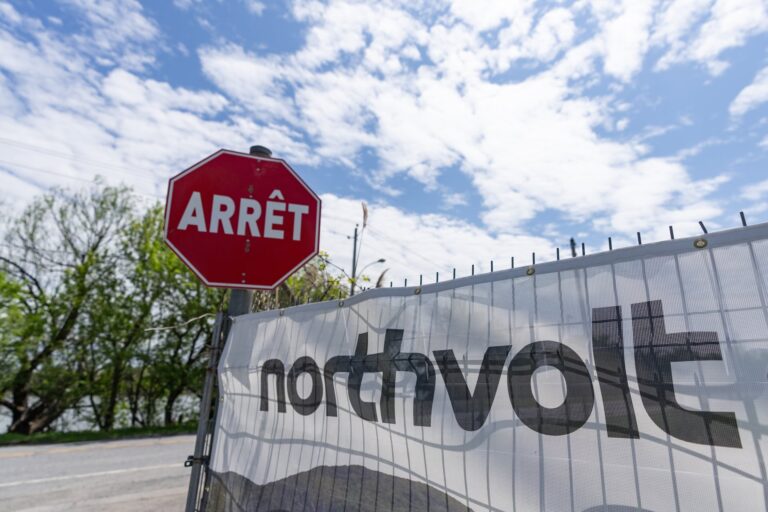 A stop sign labelled "Arrêt" is visible next to a fence with a banner displaying the text "Northvolt." Trees and a blue sky with scattered clouds are in the background.