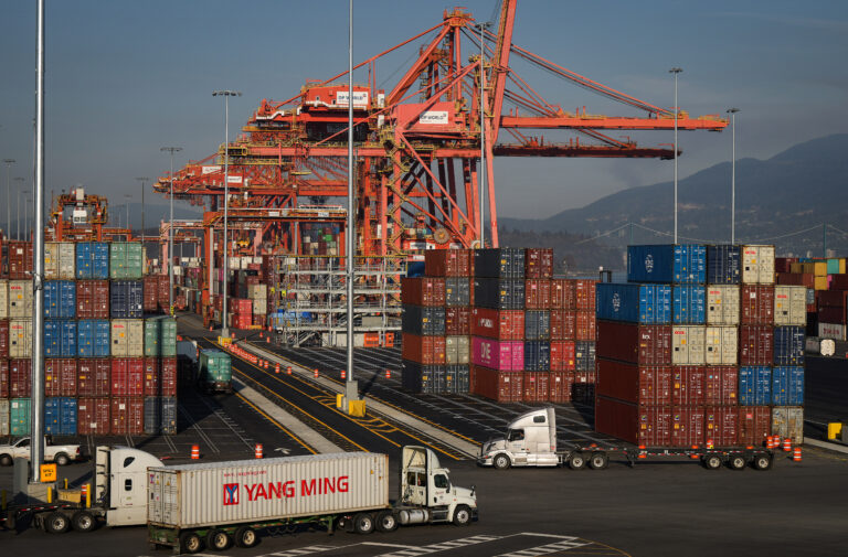 A truck carries a cargo container at the Port of Vancouver Centerm container terminal as others are stacked under gantry cranes.