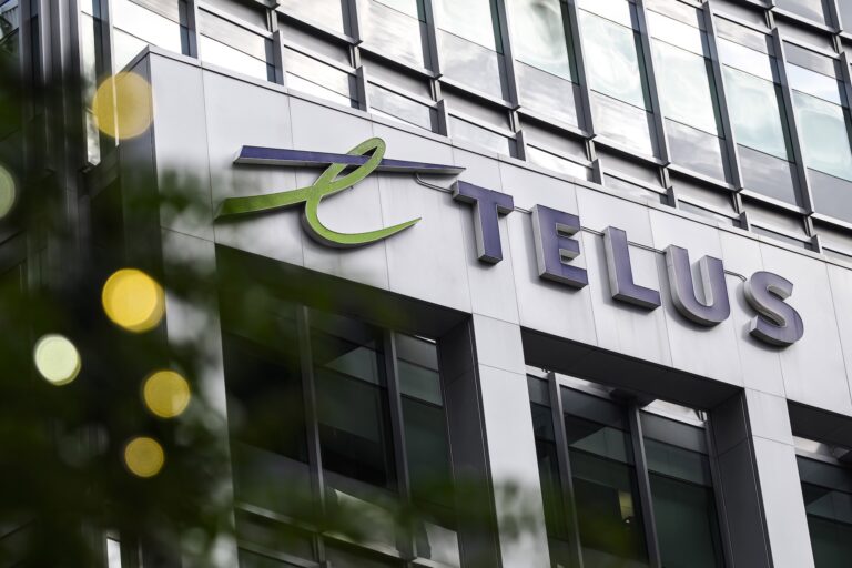 A street-level shot of a steel-and-glass office tower with Telus's corporate logo on the side of the building.