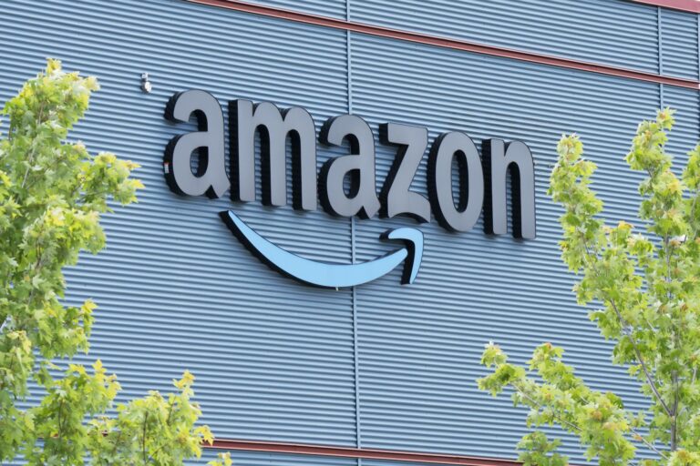 Amazon logo on the exterior of a building, surrounded by green trees.