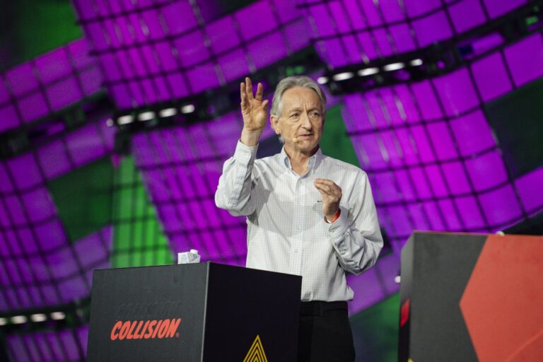 Geoffrey Hinton on stage in a dress shirt, raising one hand as he speaks