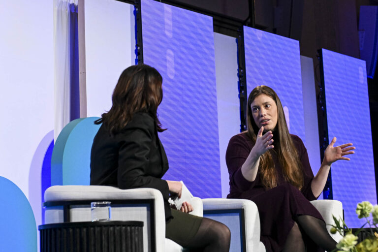 SRTX CEO Katherine Homuth and The Logic reporter Anita Balakrishnan sitting on stage in conversation, with blue panels in the background.