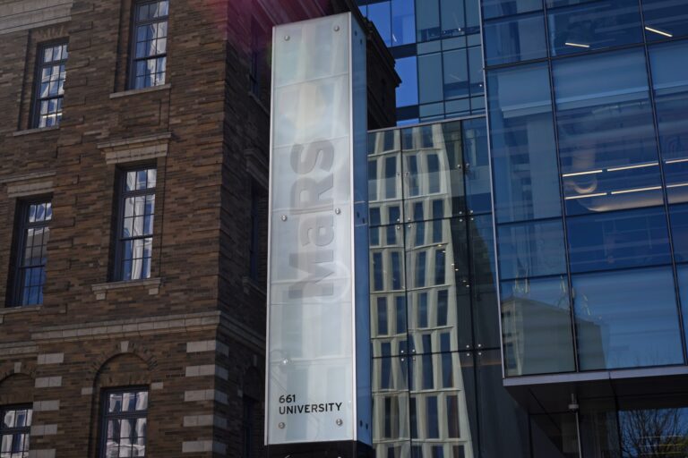Exterior of a building with a sign reading “MaRS,” featuring a mix of brick and glass architecture, and the address “661 University.”