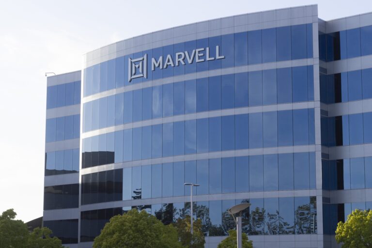 Glass facade of the Marvell company building with its logo displayed at the top, reflecting the sky and surrounding greenery.