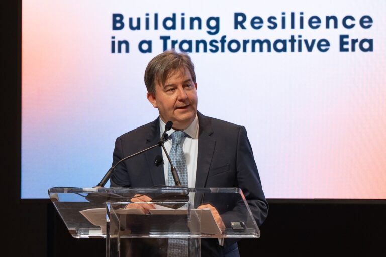 Superintendent of Financial Institutions Peter Routledge speaks on stage in front of a presentation screen that says “Building Resilience in a Transformative Era.”