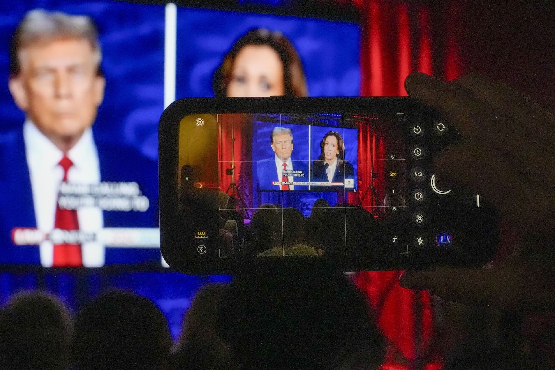 A person taking a photo of a television screen showing Republican presidential nominee Donald Trump and Democratic presidential nominee Kamala Harris speaking at the presidential debate.