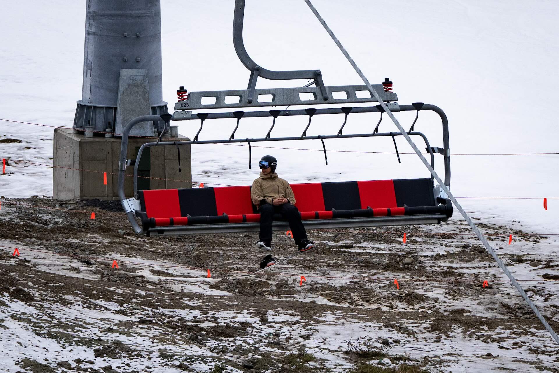 Person seated on a stationary ski lift chair above a rocky, snow-dusted terrain.